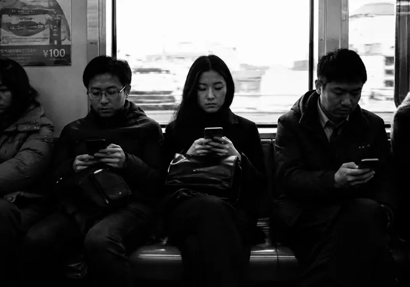 Commuters sitting side by side on a train, each looking at their phone